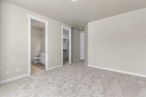 Unfurnished bedroom with light colored carpet, connected bathroom, a spacious closet, and a closet