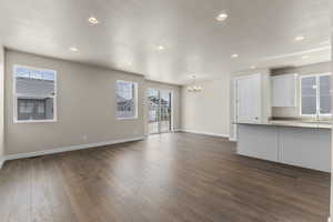 Unfurnished living room with plenty of natural light, dark wood-type flooring, a chandelier, and a textured ceiling