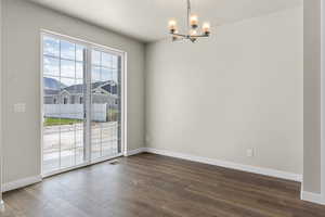 Empty room featuring dark hardwood / wood-style flooring, plenty of natural light, and an inviting chandelier