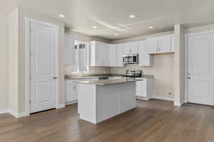 Kitchen featuring appliances with stainless steel finishes, white cabinetry, sink, dark hardwood / wood-style floors, and a kitchen island