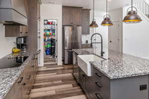 Kitchen with an island with sink, stainless steel appliances, custom exhaust hood, decorative backsplash, and hardwood / wood-style flooring