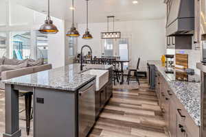 Kitchen featuring stainless steel dishwasher, a kitchen island with sink, light stone countertops, black electric cooktop, and hardwood / wood-style flooring