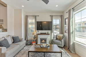 Living room with ceiling fan, a stone fireplace, and light hardwood / wood-style flooring