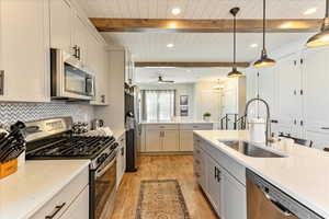 Kitchen with light wood-type flooring, appliances with stainless steel finishes, beam ceiling, decorative light fixtures, and sink