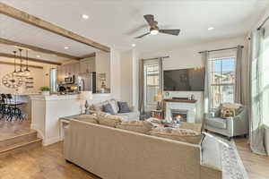 Living room with beamed ceiling, ceiling fan, light hardwood / wood-style floors, and a fireplace