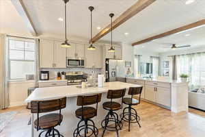 Kitchen featuring decorative light fixtures, stainless steel appliances, backsplash, a center island with sink, and beam ceiling