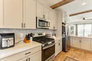 Kitchen with white cabinetry, light wood-type flooring, stainless steel appliances, beam ceiling, and ceiling fan