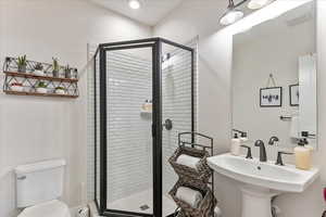 Bathroom featuring sink, a shower with shower door, and toilet