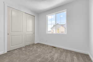 Unfurnished bedroom with a closet, a textured ceiling, and light carpet