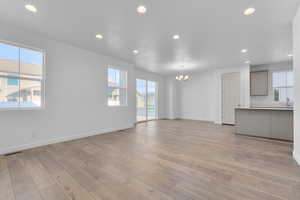 Unfurnished living room featuring an inviting chandelier, light wood-type flooring, plenty of natural light, and sink