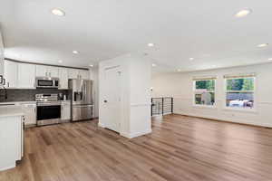 Kitchen with white cabinetry, stainless steel appliances, tasteful backsplash, and light wood-type flooring