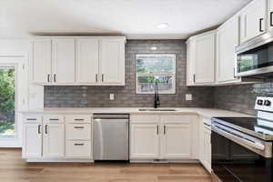 Kitchen featuring decorative backsplash, appliances with stainless steel finishes, light hardwood / wood-style flooring, and white cabinets