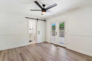 Unfurnished bedroom featuring access to outside, light hardwood / wood-style flooring, a barn door, and ensuite bathroom