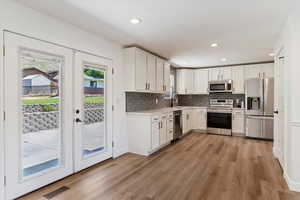 Kitchen with white cabinetry, light hardwood / wood-style floors, french doors, and appliances with stainless steel finishes