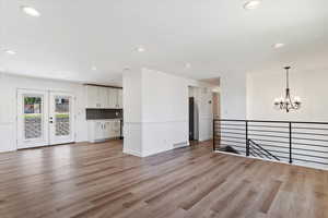 Unfurnished living room featuring an inviting chandelier, french doors, and hardwood / wood-style floors