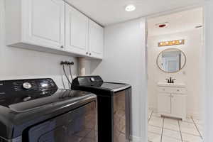 Clothes washing area featuring washer and clothes dryer, sink, cabinets, and light tile patterned floors