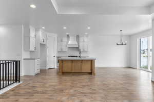 Kitchen featuring a center island with sink, premium range hood, white cabinetry, and light hardwood / wood-style floors