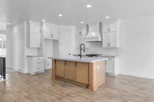 Kitchen featuring light hardwood / wood-style floors, white cabinetry, sink, premium range hood, and an island with sink