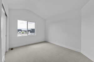 Unfurnished room featuring light carpet and vaulted ceiling