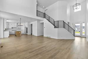 Unfurnished living room featuring light hardwood / wood-style flooring, a towering ceiling, sink, and an inviting chandelier