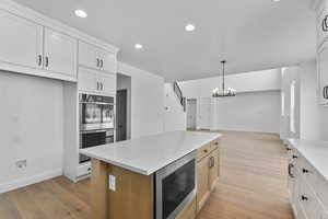 Kitchen with light stone counters, stainless steel appliances, a chandelier, light hardwood / wood-style floors, and white cabinetry