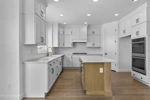 Kitchen with white cabinets, wood-type flooring, double oven, and a center island