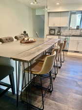 Kitchen featuring a breakfast bar area, white cabinetry, dishwasher, backsplash, and dark hardwood / wood-style floors