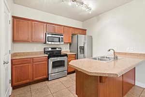 Kitchen with track lighting, stainless steel appliances, sink, kitchen peninsula, and light tile patterned floors