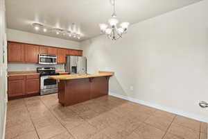 Kitchen featuring stainless steel appliances, hanging light fixtures, light tile patterned floors, rail lighting, and a notable chandelier