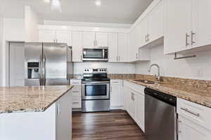 Kitchen featuring stainless steel appliances, white cabinets, sink, light stone countertops, and dark hardwood / wood-style floors