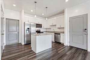 Kitchen featuring appliances with stainless steel finishes, white cabinetry, a center island, and dark wood-type flooring