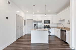 Kitchen with white cabinets, a center island, dark hardwood / wood-style flooring, stainless steel appliances, and decorative light fixtures