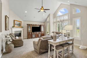 Carpeted living room featuring ceiling fan, a tile fireplace, and high vaulted ceiling