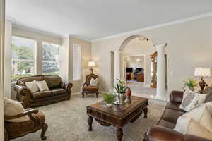 Carpeted living room featuring crown molding and ornate columns