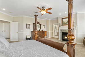 Bedroom with carpet floors, ceiling fan, ensuite bathroom, a tiled fireplace, and ornamental molding