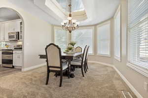 Dining space featuring a notable chandelier, light hardwood / wood-style flooring, ornamental molding, and a tray ceiling