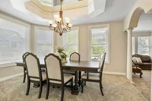 Carpeted dining space featuring ornamental molding, a notable chandelier, a healthy amount of sunlight, and a raised ceiling