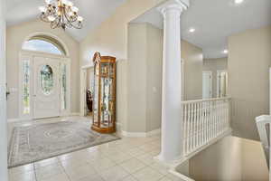 Tiled foyer with a notable chandelier, decorative columns, and lofted ceiling