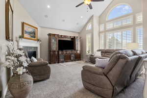 Carpeted living room with a fireplace, high vaulted ceiling, and ceiling fan