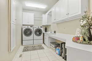 Laundry area with light tile patterned flooring, washer and clothes dryer, sink, and cabinets