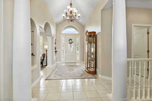 Tiled foyer entrance with a notable chandelier, decorative columns, and vaulted ceiling