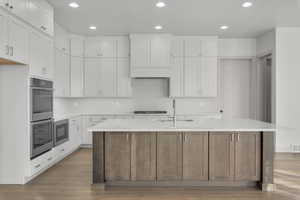 Kitchen with a center island with sink, white cabinetry, and double oven