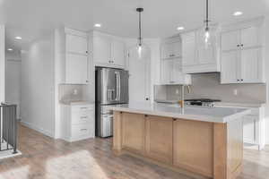 Kitchen featuring white cabinets, stainless steel fridge with ice dispenser, a kitchen island with sink, and sink