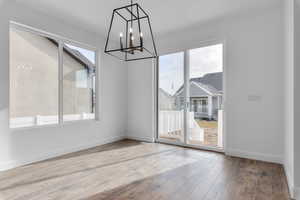 Unfurnished dining area featuring wood-type flooring and an inviting chandelier