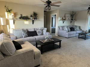 Living room with ceiling fan, light colored carpet, and a textured ceiling