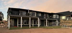 Back house at dusk featuring a balcony and a yard