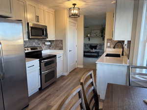 Kitchen with stainless steel appliances, hanging light fixtures, sink, hardwood / wood-style flooring, and white cabinets