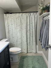 Full bathroom with toilet, vanity, a textured ceiling, shower / tub combo, and hardwood / wood-style flooring