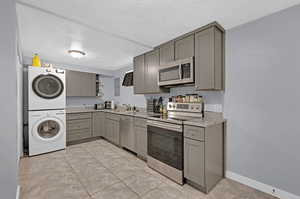 Basement kitchen featuring light tile patterned floors, light stone counters, appliances with stainless steel finishes, sink, and gray cabinetry