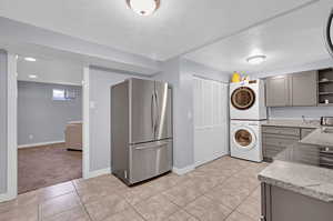 Kitchen with gray cabinets, light tile patterned flooring, stacked washer and dryer, and stainless steel refrigerator